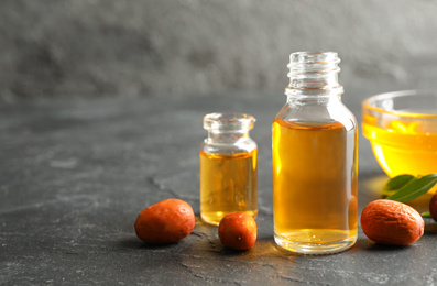 Photo of Jojoba oil and seeds on dark grey table