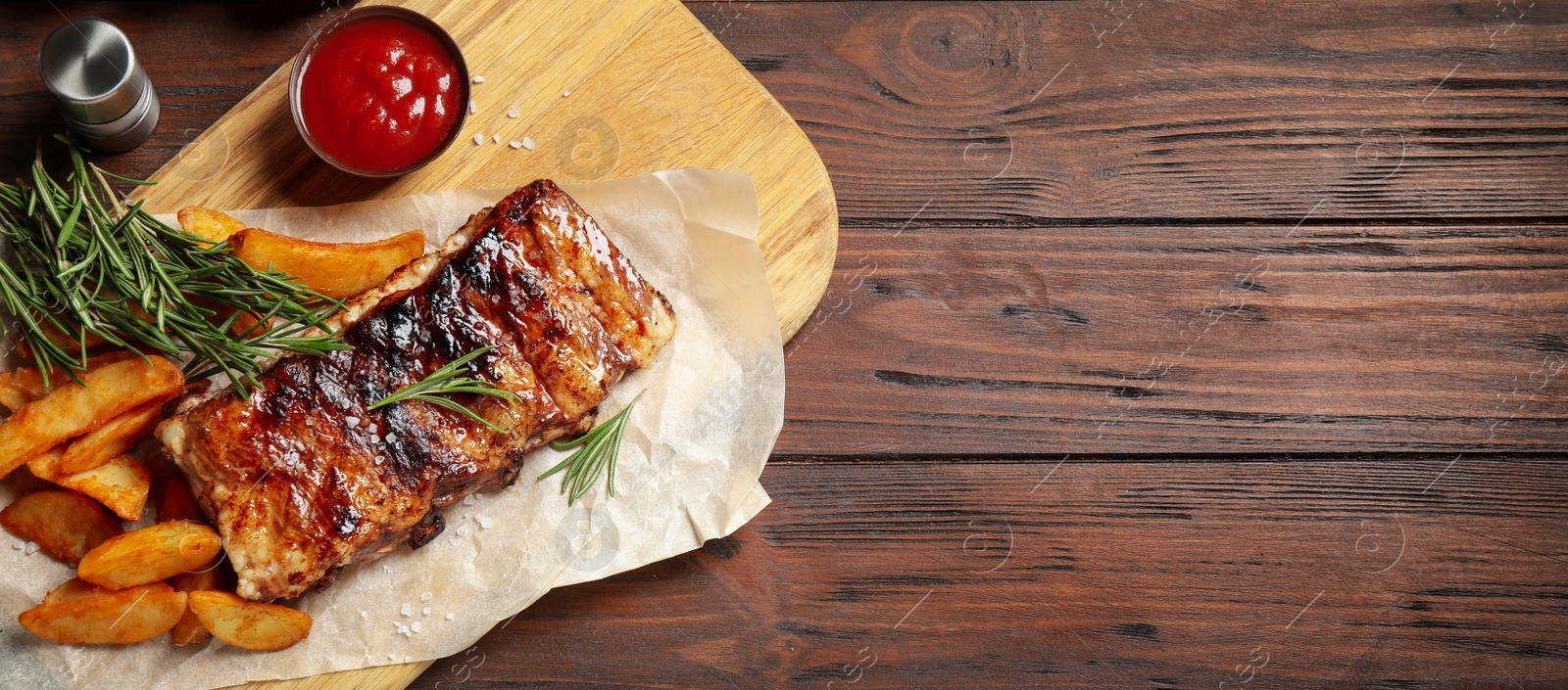 Image of Delicious grilled ribs and garnish on wooden table, top view with space for text. Banner design