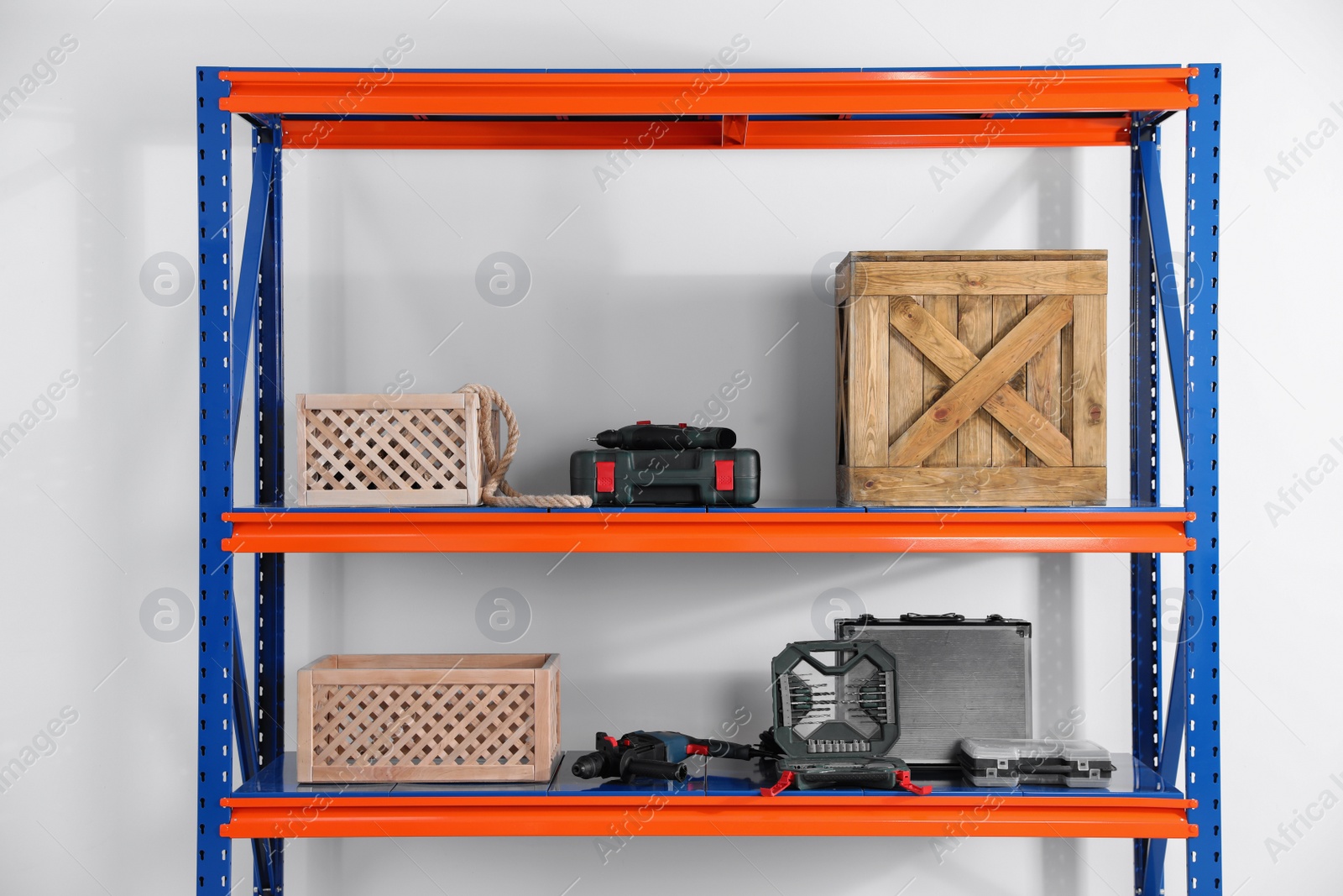 Photo of Metal shelving unit with wooden crates and different instruments on light background