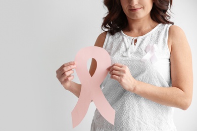 Woman holding pink paper ribbon against white background, closeup. Breast cancer awareness concept