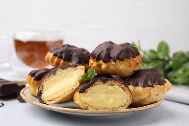 Photo of Delicious profiteroles with chocolate spread and cream on white table, closeup