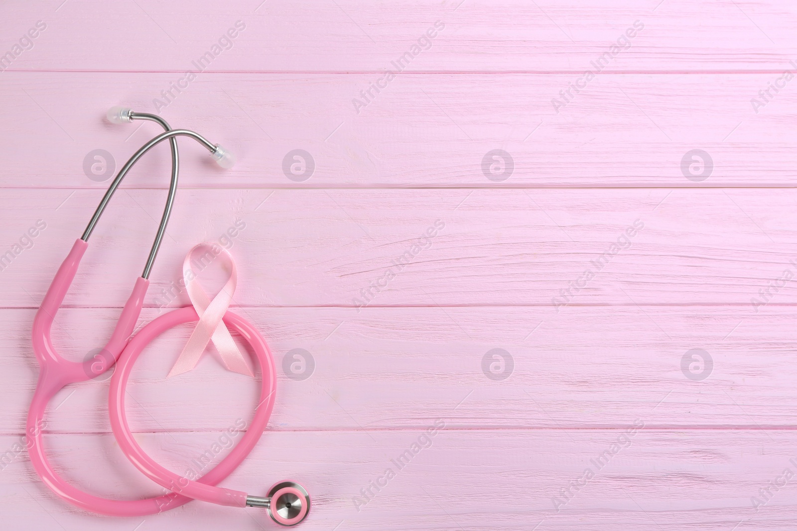 Photo of Pink ribbon and stethoscope on wooden background, flat lay with space for text. Breast cancer concept