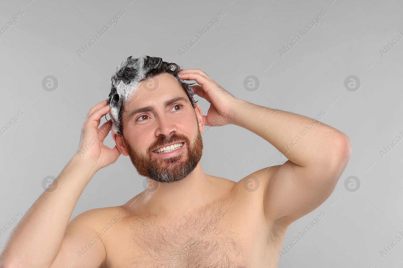 Photo of Happy man washing his hair with shampoo on grey background