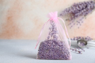 Photo of Scented sachet with dried lavender flowers on light gray table, space for text