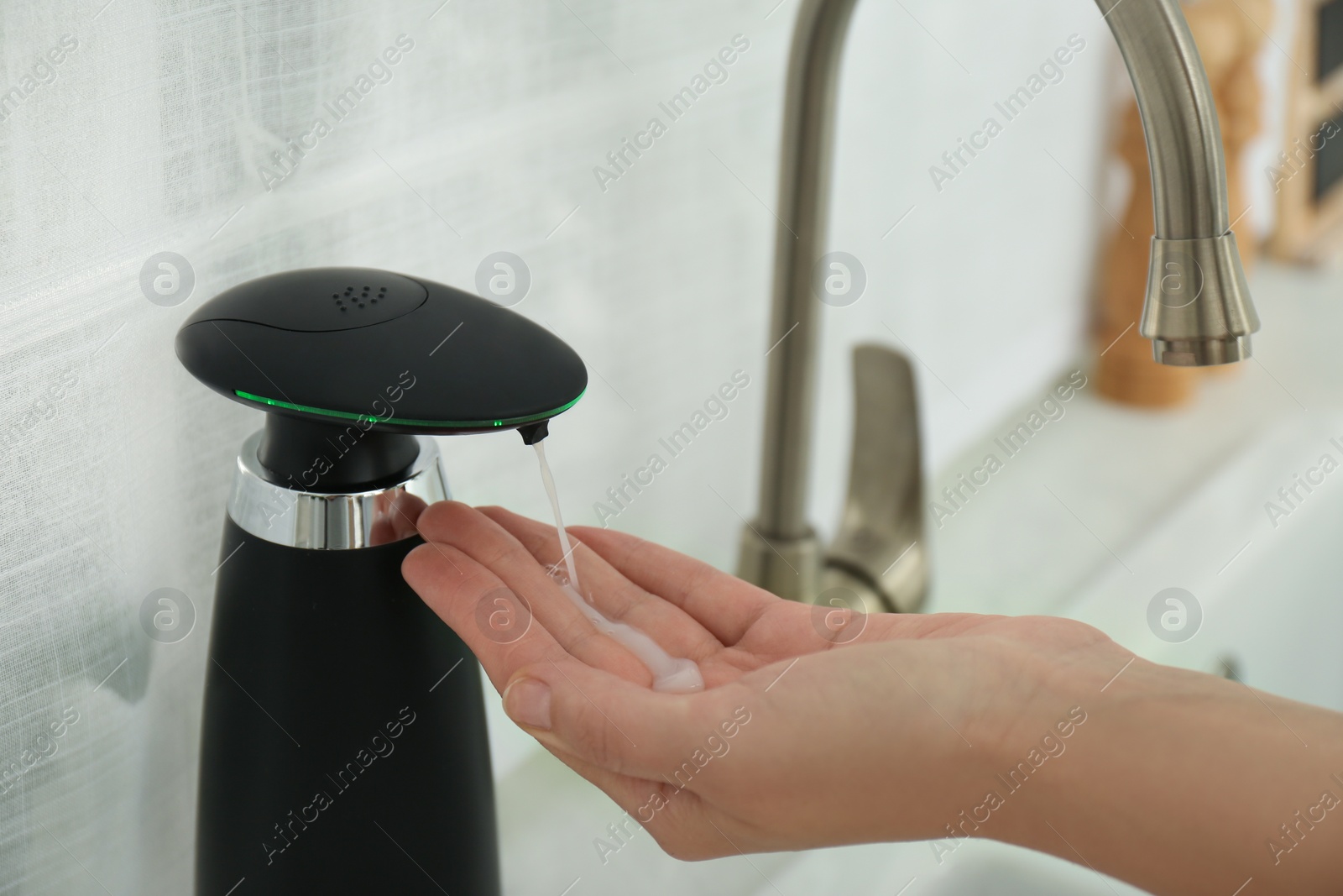 Photo of Woman using automatic soap dispenser in kitchen, closeup