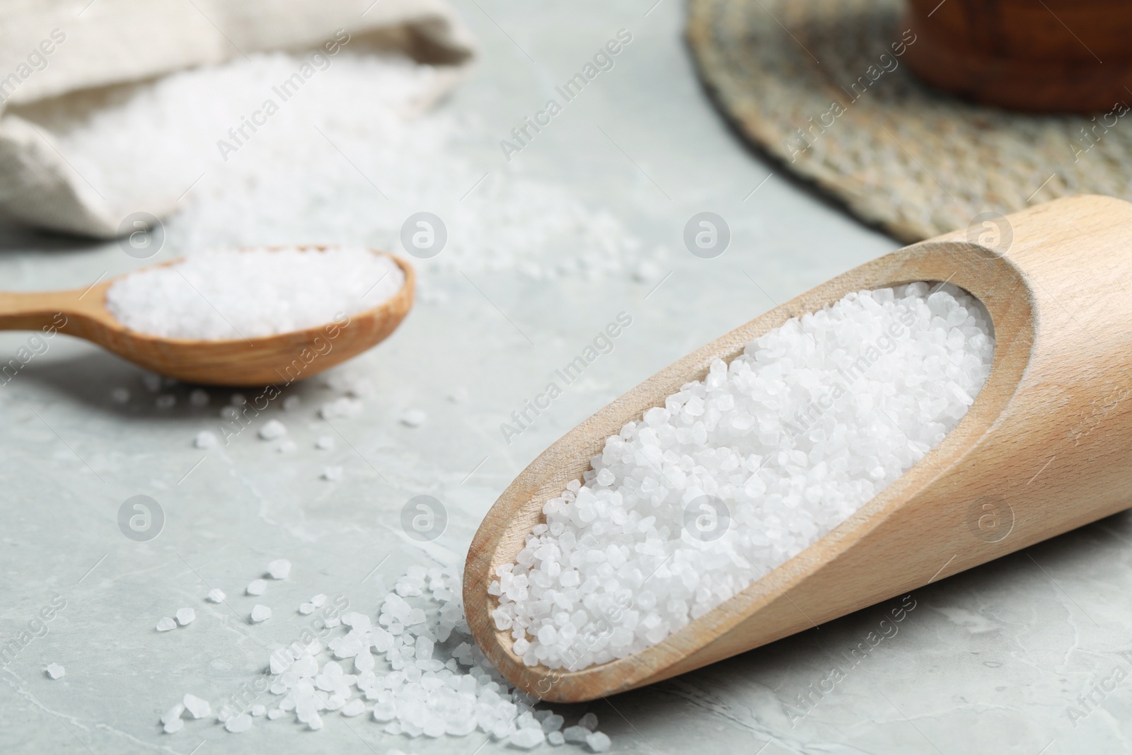 Photo of Natural sea salt in wooden scoop on light grey marble table, closeup