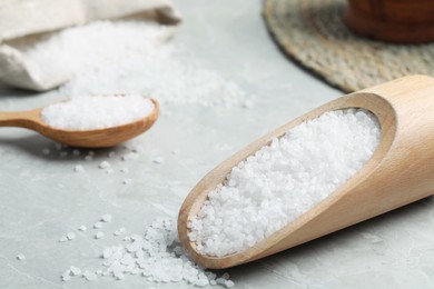 Natural sea salt in wooden scoop on light grey marble table, closeup