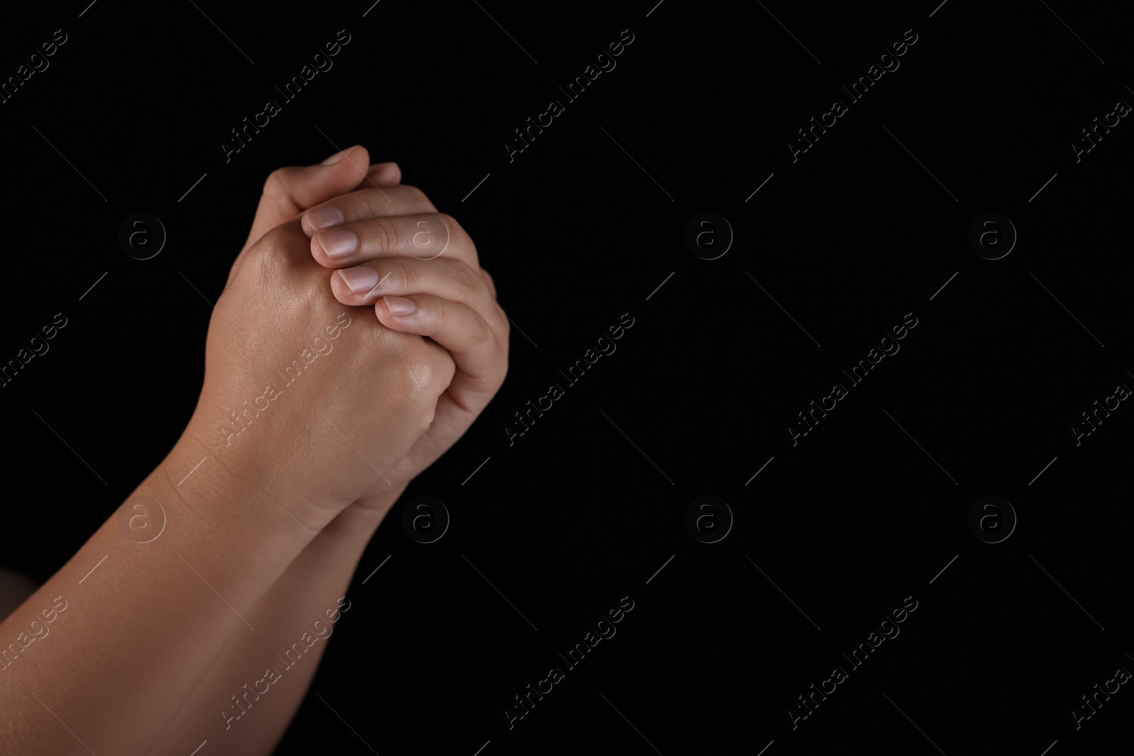 Photo of Woman holding hands clasped while praying on black background, closeup. Space for text