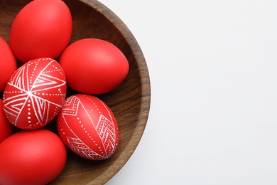 Photo of Wooden bowl with painted red Easter eggs on white background, top view