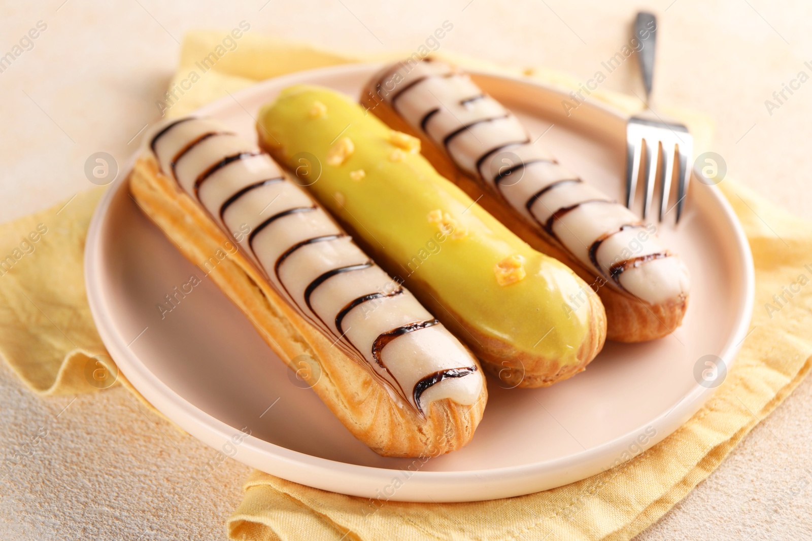 Photo of Different tasty glazed eclairs served on color textured table, closeup