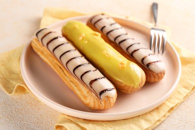 Different tasty glazed eclairs served on color textured table, closeup