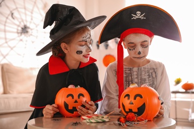 Photo of Cute little kids with pumpkin candy buckets wearing Halloween costumes at home