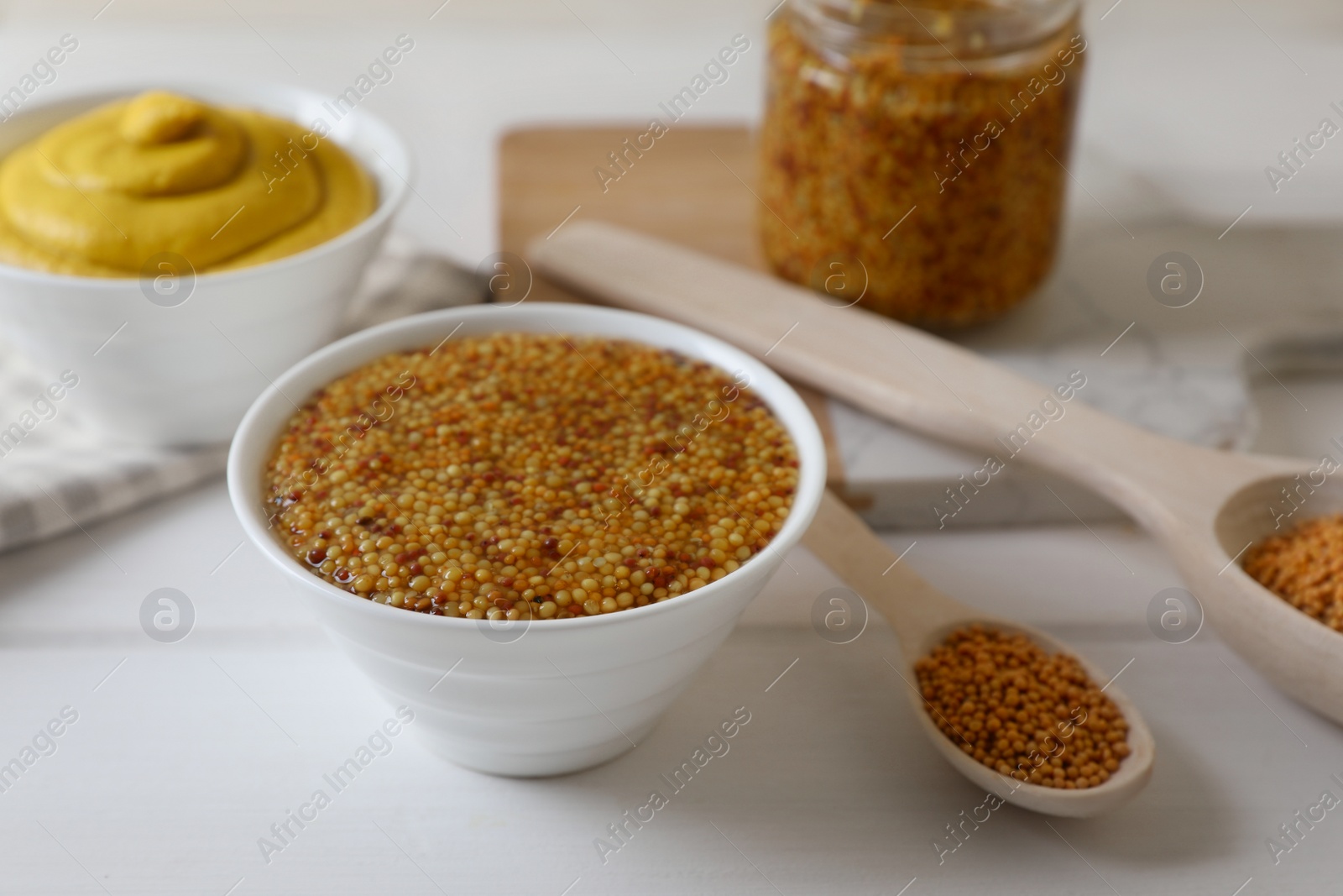 Photo of Bowl and spoons of whole grain mustard on white wooden table