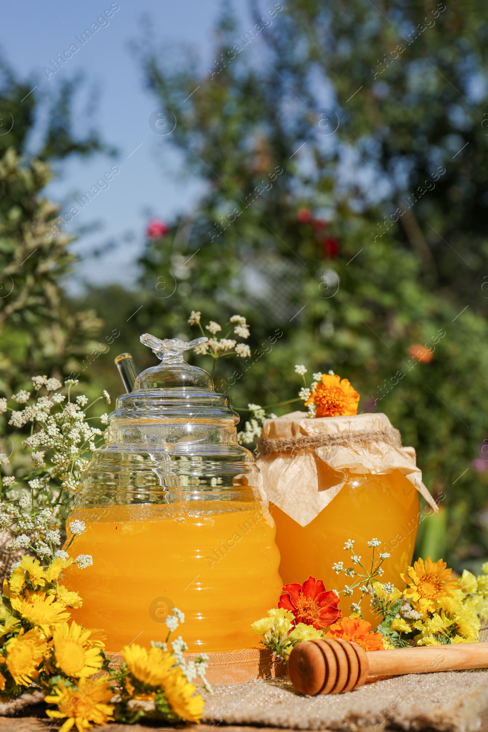 Photo of Delicious fresh honey and beautiful flowers on wooden table in garden