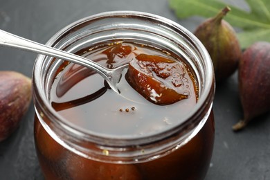 Photo of Jar of tasty sweet jam and fresh figs on black table, closeup