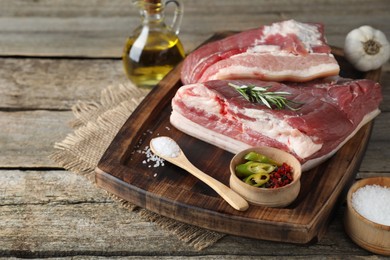 Pieces of raw pork belly, salt, oil, garlic and rosemary on wooden table