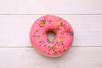 Photo of Glazed donut decorated with sprinkles on white wooden table, top view. Tasty confectionery