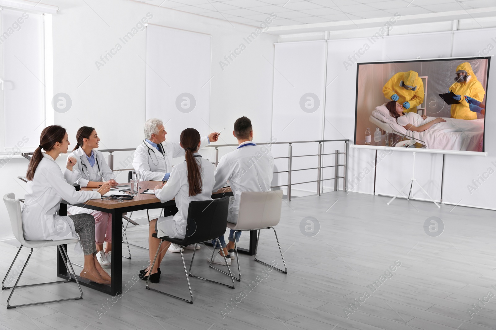 Image of Team of doctors using video projector during coronavirus conference in office