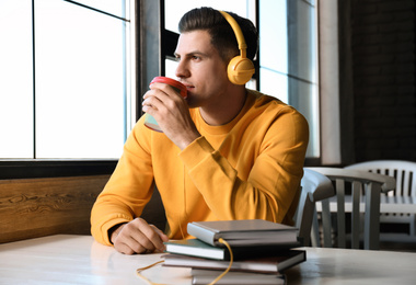 Photo of Man with headphones connected to book at table in cafe