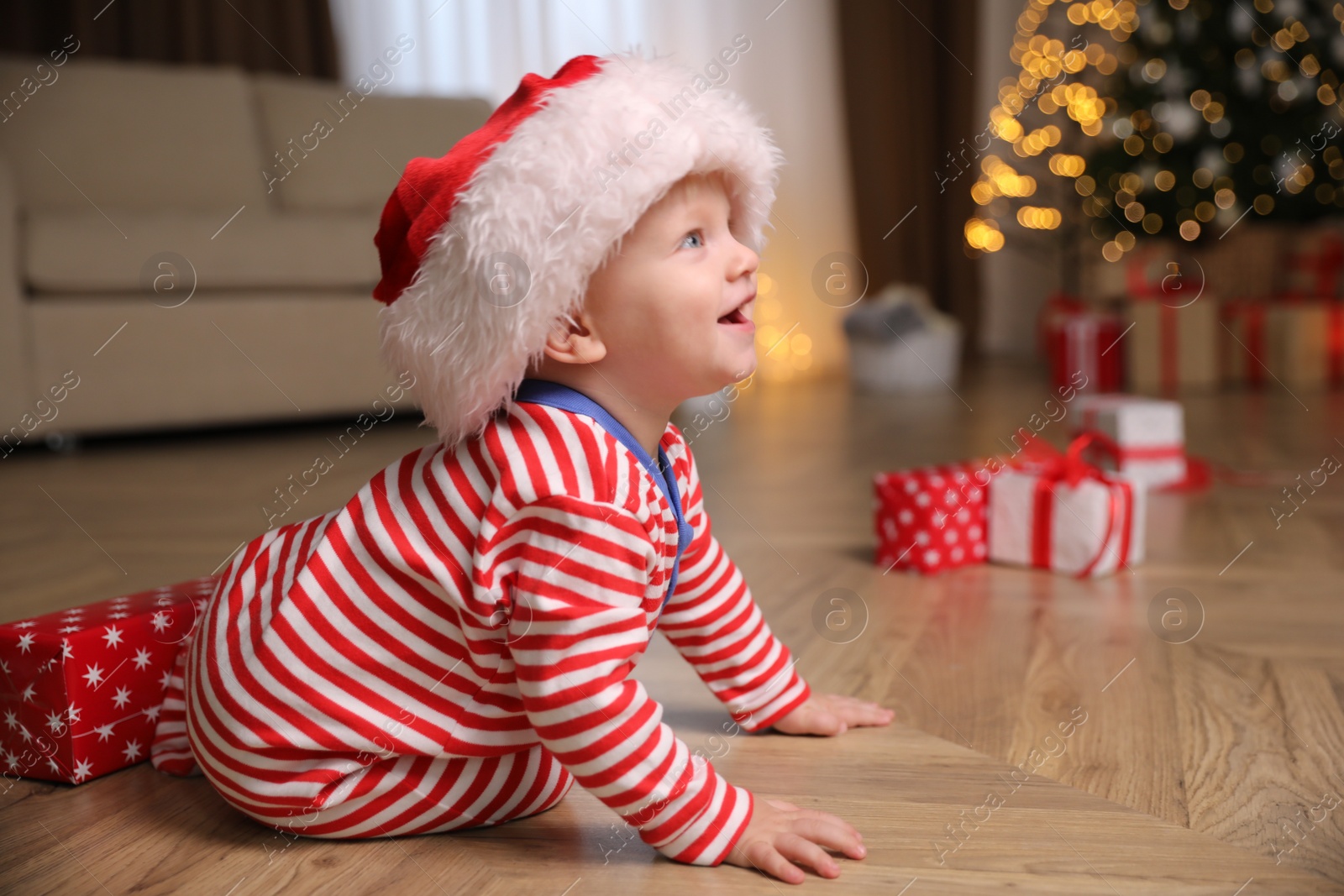 Photo of Baby in Christmas pajamas and Santa hat near gift box  indoors