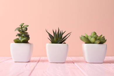 Photo of Artificial plants in white flower pots on pink wooden table