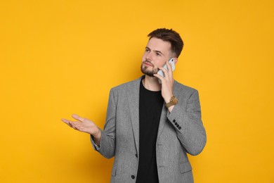 Photo of Handsome man in stylish grey jacket talking on phone against yellow background