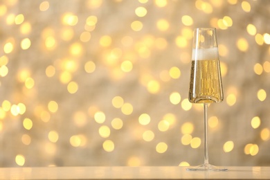 Photo of Glass of fizzy champagne on table against blurred fairy lights, space for text