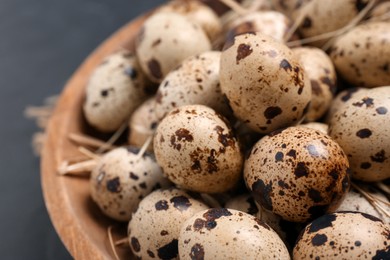 Photo of Bowl with quail eggs and straw on black table, closeup