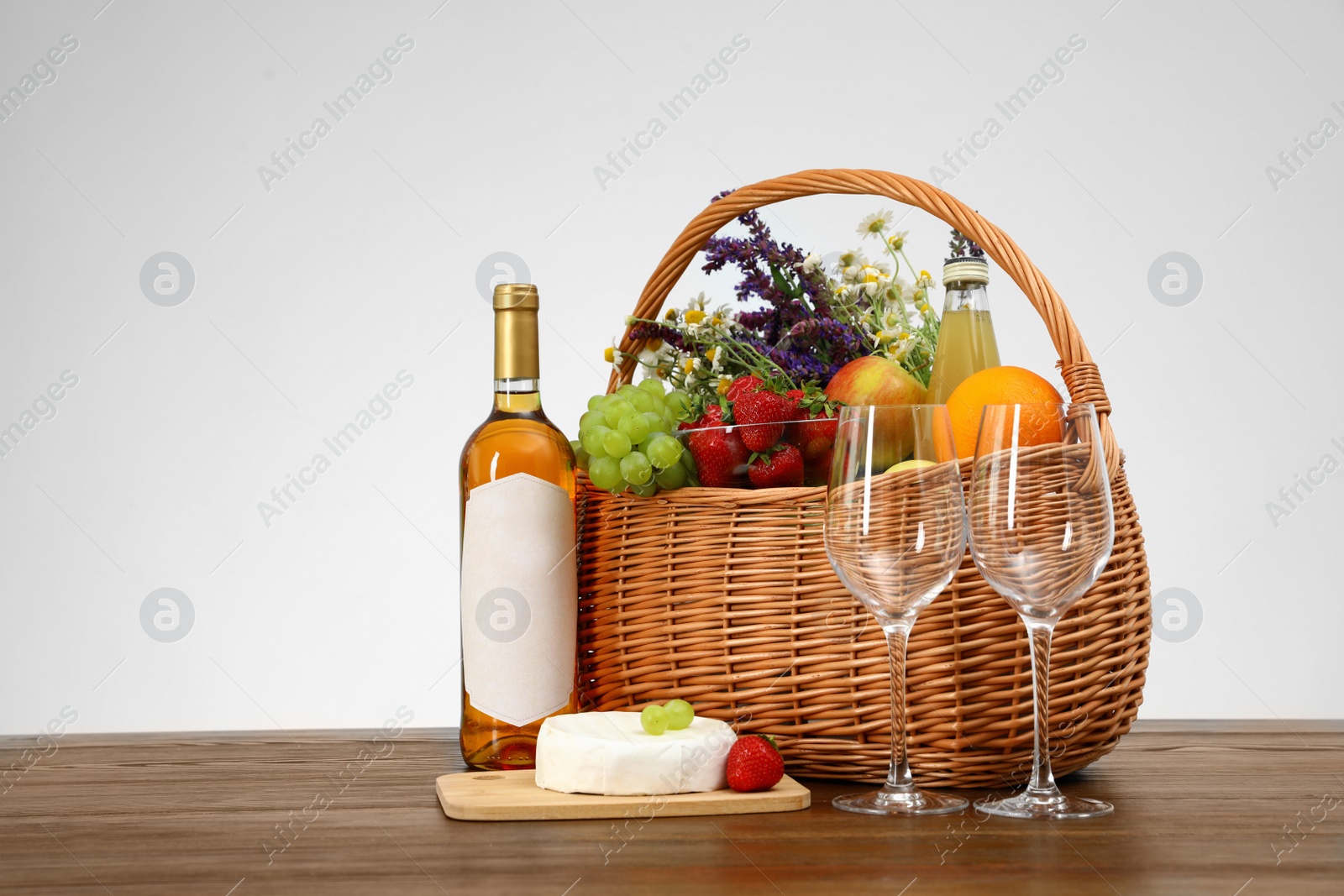 Photo of Picnic basket with wine and products on wooden table against white background. Space for text