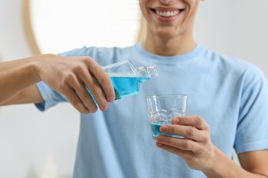 Young man using mouthwash indoors, closeup view