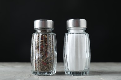 Photo of Salt and pepper shakers on light table against black background, closeup