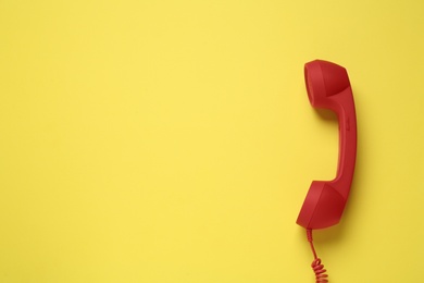 Photo of Red corded telephone handset on yellow background, top view. Hotline concept