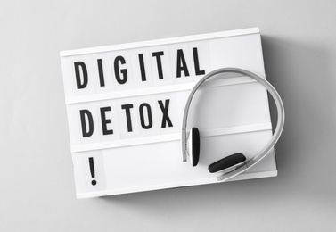 Photo of Lightbox with words DIGITAL DETOX and headphones on light grey background, top view