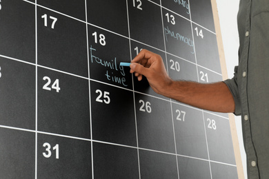 Photo of Man writing with chalk on board calendar, closeup of hand