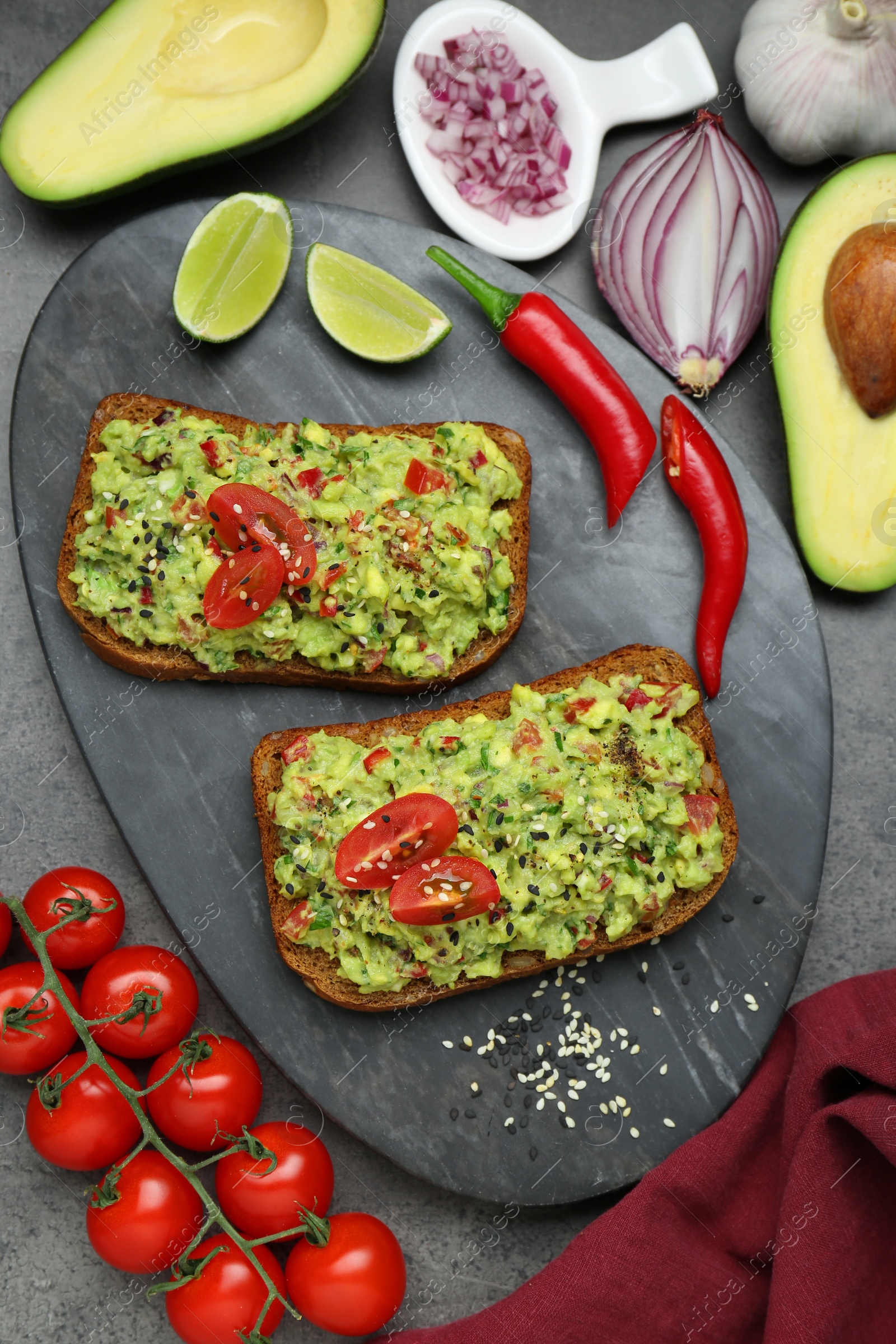 Photo of Slices of bread with tasty guacamole and ingredients on grey table, flat lay