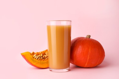 Photo of Tasty pumpkin juice in glass, whole and cut pumpkins on pink background