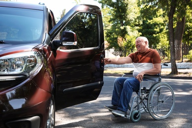 Photo of Senior man in wheelchair opening door of his van outdoors