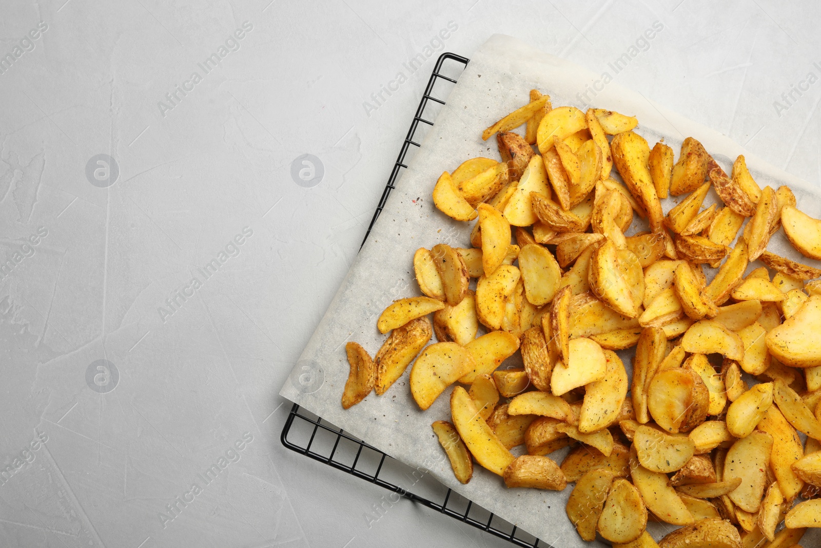 Photo of Cooling rack with delicious oven baked potatoes on grey background, top view. Space for text