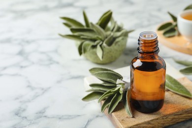 Photo of Bottle of essential sage oil and leaves on white marble table. Space for text