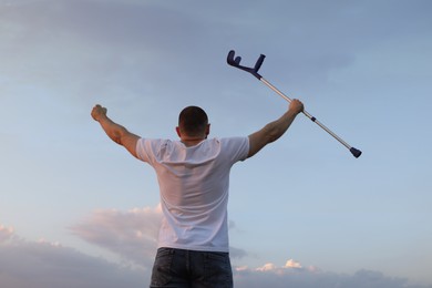 Photo of Man raising elbow crutch up to sky, back view. Healing miracle