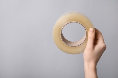 Photo of Woman holding transparent adhesive tape on light grey background, closeup. Space for text
