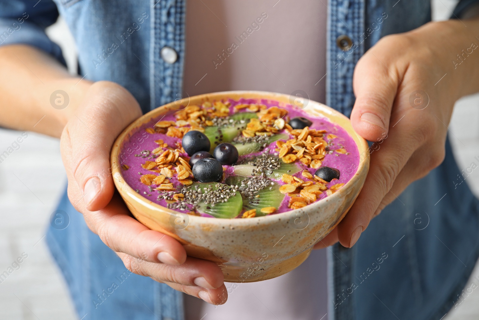 Photo of Woman holding bowl of acai smoothie with granola and berries, closeup