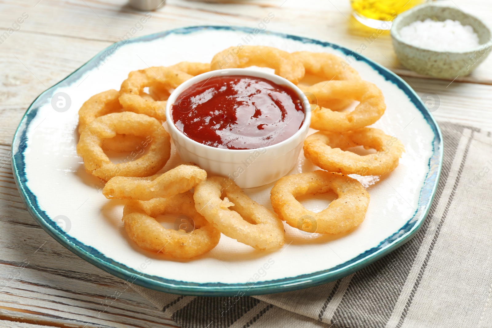 Photo of Plate with fried onion rings and sauce on table