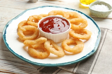 Photo of Plate with fried onion rings and sauce on table