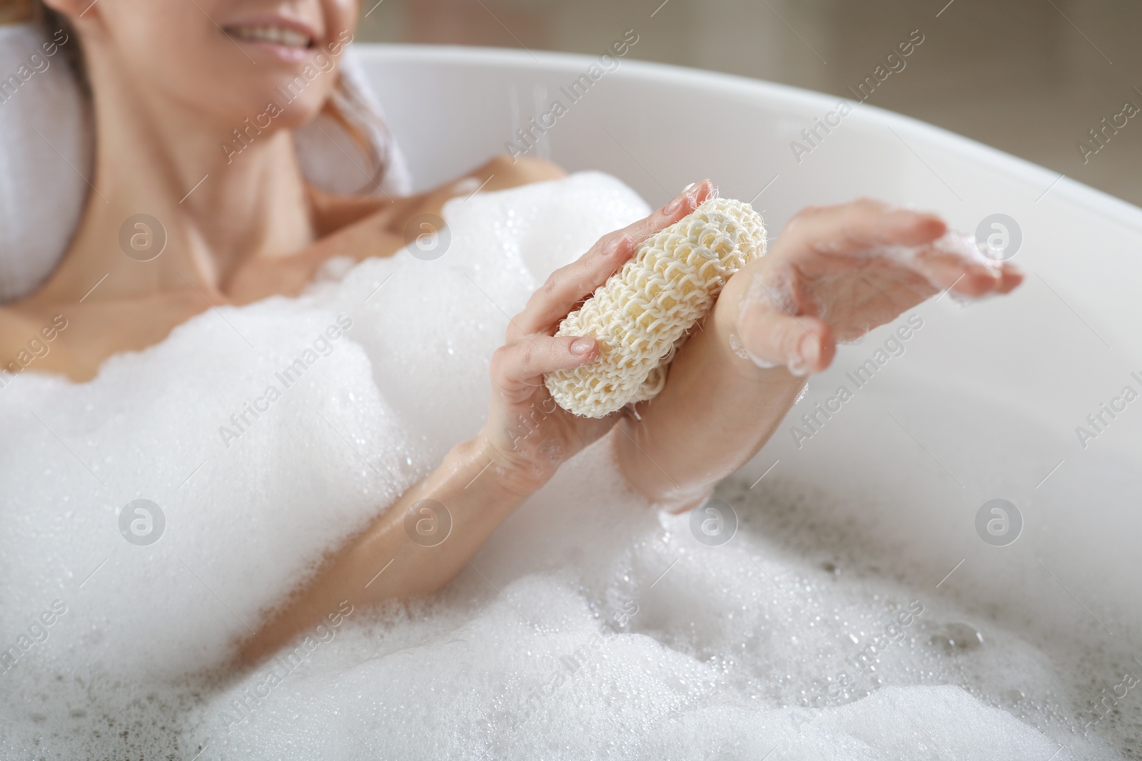 Photo of Woman rubbing her forearm with sponge while taking bath, closeup