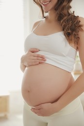 Photo of Pregnant woman touching her belly indoors, closeup