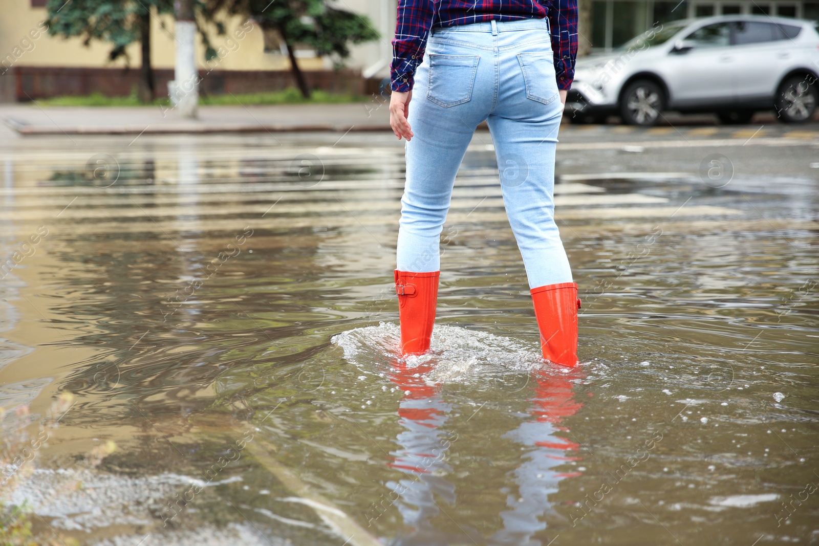 Photo of Woman with red rubber boots in puddle, closeup. Rainy weather