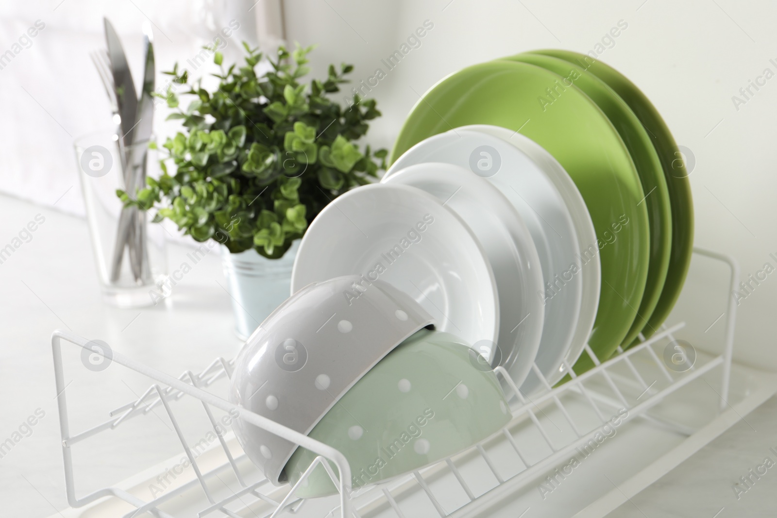 Photo of Drainer with different clean dishware and houseplant on light table in kitchen