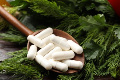 Photo of Dietary supplements. Spoon with pills, dill and parsley on table, closeup