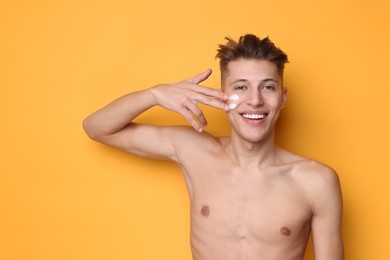 Photo of Handsome man applying moisturizing cream onto his face on orange background. Space for text